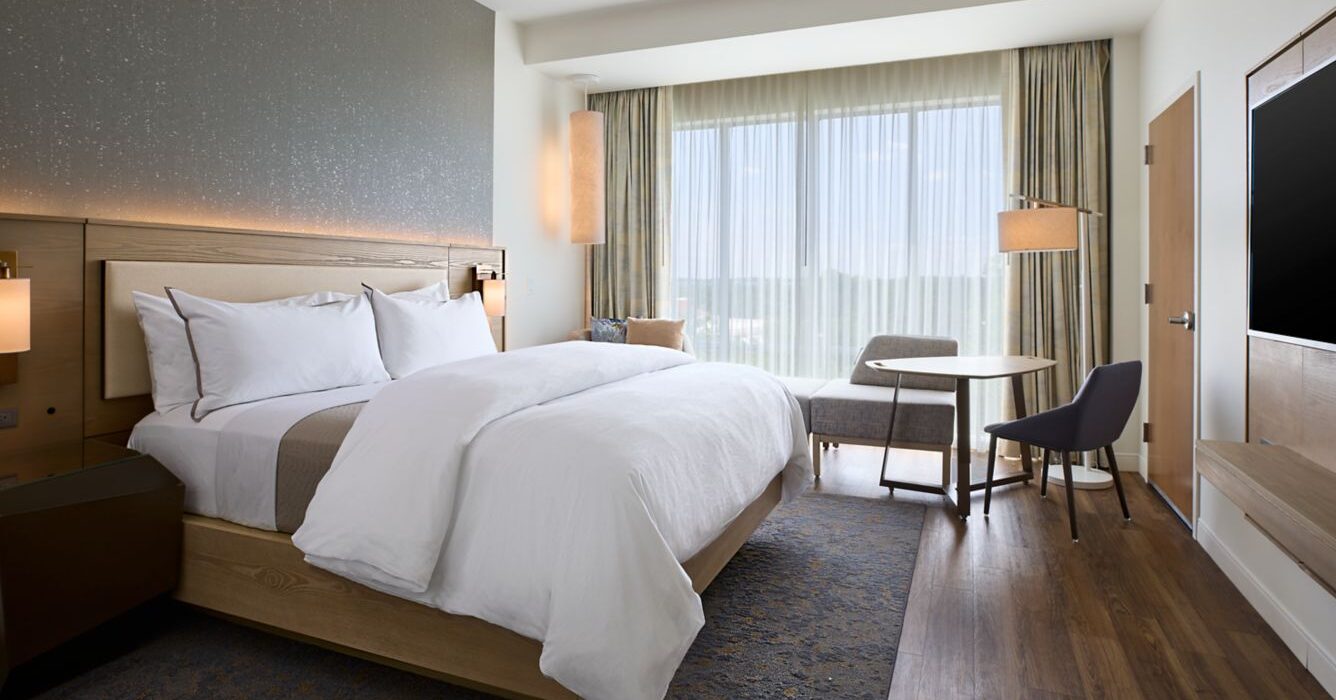 Modern hotel room with a king bed and large windows.