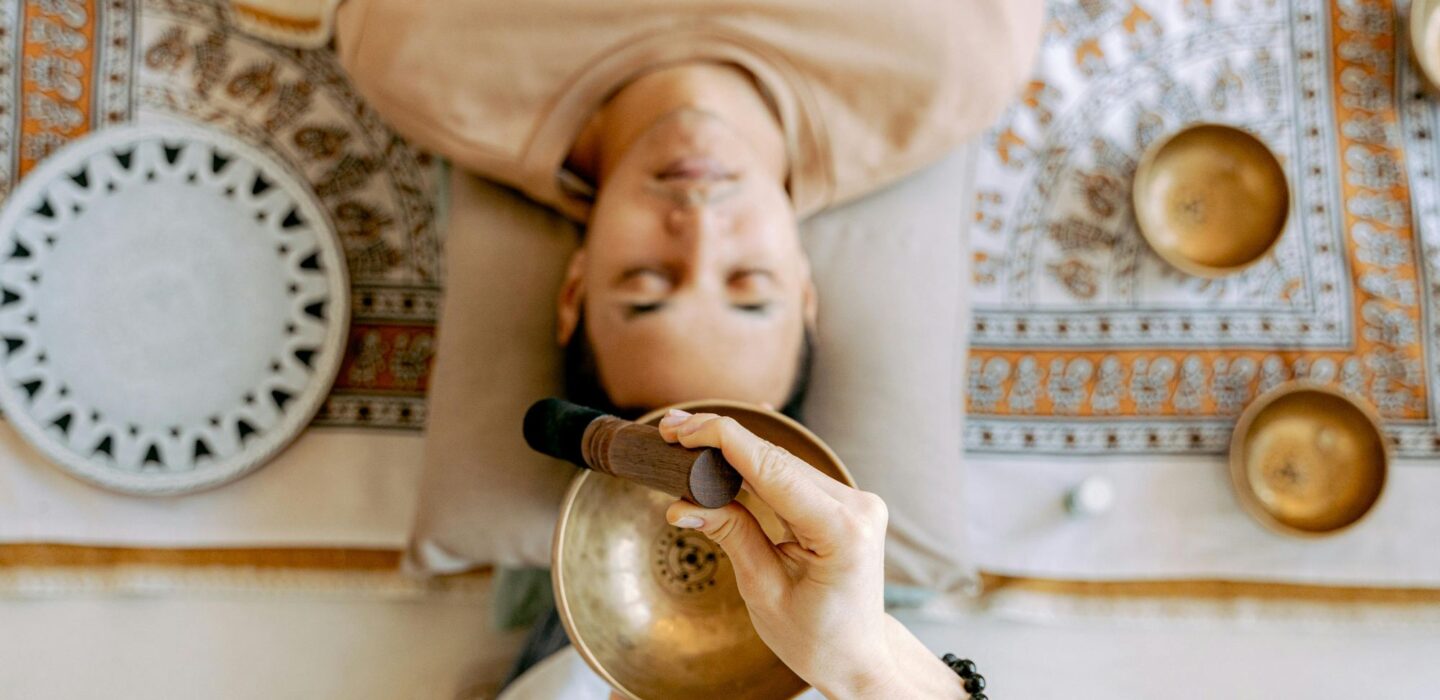 Person lying down with eyes closed during a sound healing session using a singing bowl.